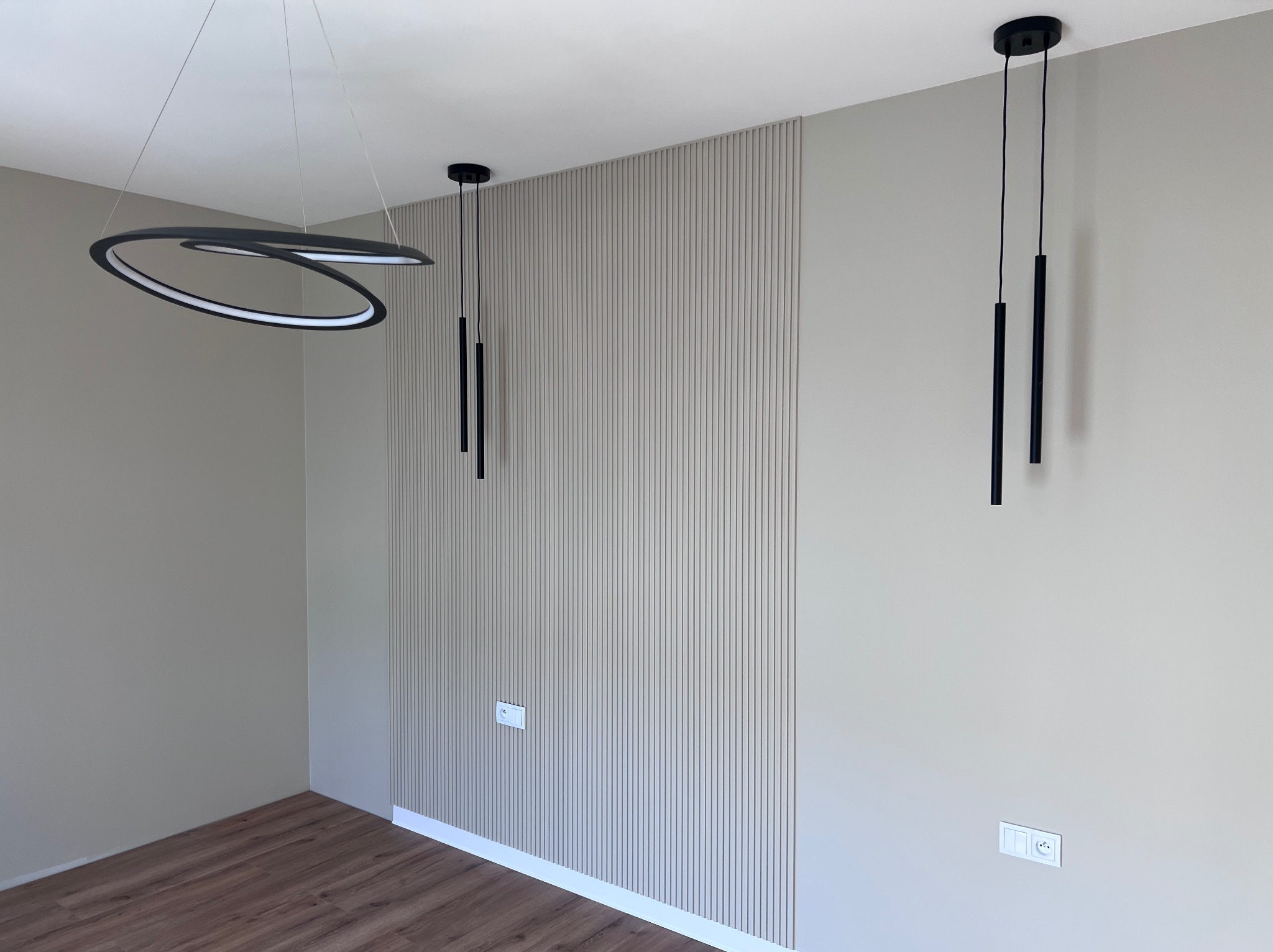 Nowoczesne wykończenie wnętrza: panel ścienny z pionowymi listwami w odcieniach beżu, designerskie lampy wiszące i drewnopodobna podłoga. Minimalistyczny styl.