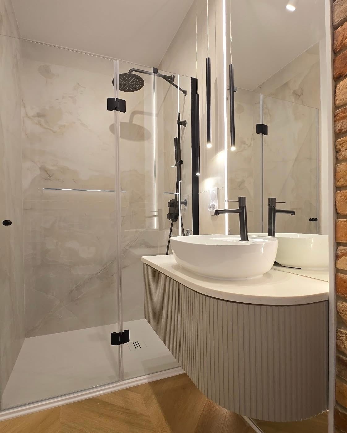 Nowoczesna łazienka z kabiną typu walk-in, umywalką nablatową i minimalistycznym oświetleniem. Ściana z cegły dodaje surowego charakteru.