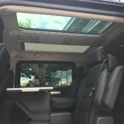 Wnętrze przestronnego, czarnego vana z rozkładanym stolikiem i panoramicznym oknem dachowym, widok z boku na fotele pasażerów.