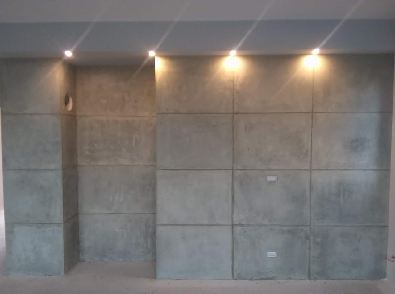 Ściana w Krakowie wykończona płytami imitującymi beton, podświetlona punktowymi lampami sufitowymi, z widocznym otworem instalacyjnym.