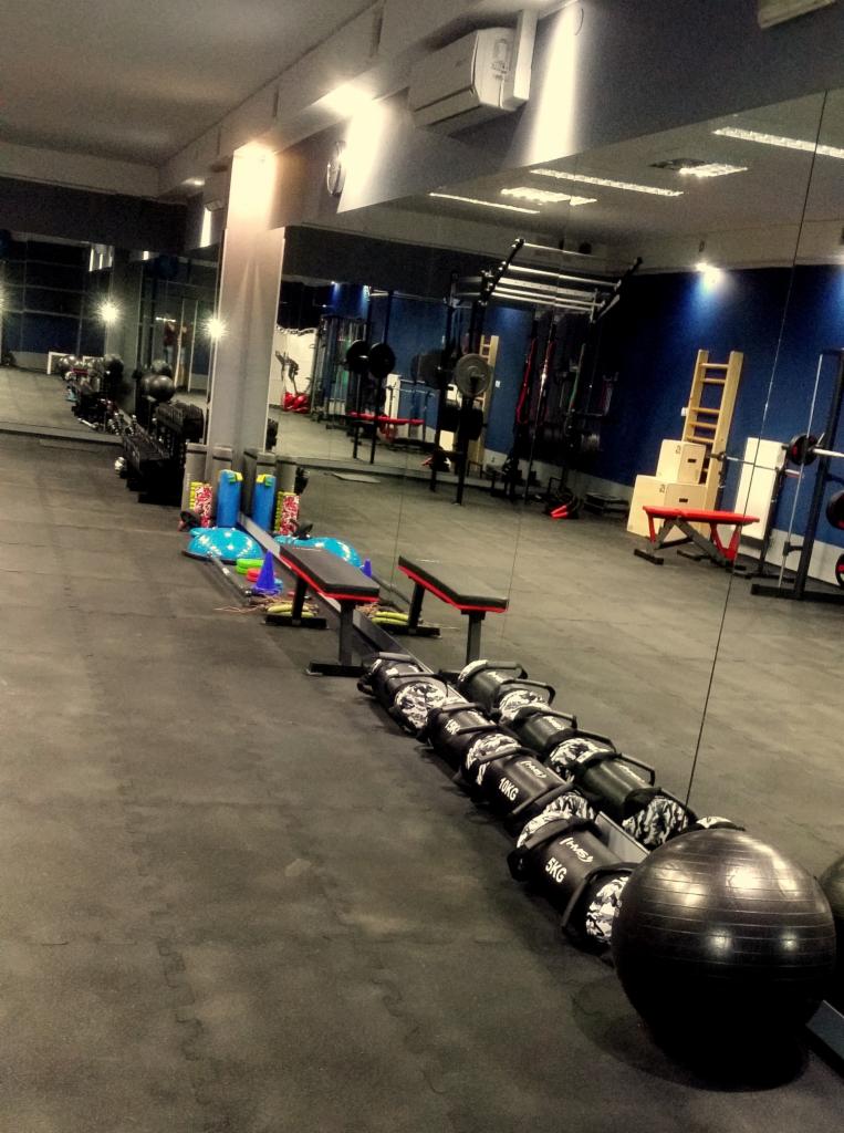 Wnętrze siłowni z rzędem worków obciążeniowych z kamuflażem, piłką do ćwiczeń i sprzętem do treningu siłowego w tle, widok z perspektywy podłogi.