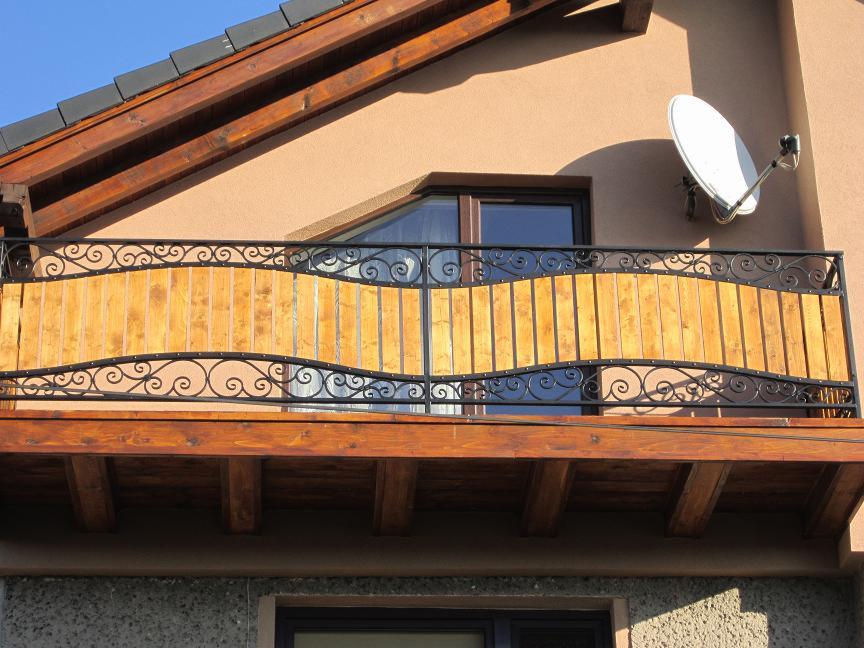 Balkon z ozdobną, kutą balustradą z drewnianym wypełnieniem, widok z dołu, na elewacji budynku widoczna antena satelitarna.