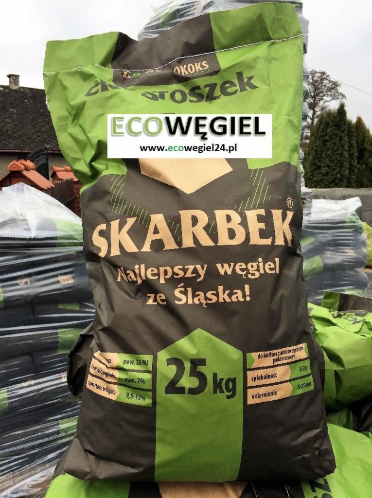 Stos worków z ekogroszkiem SKARBEK, z napisem 'Najlepszy węgiel ze Śląska!' i adresem strony internetowej ecowegiel24.pl, na tle zabudowań i zieleni.