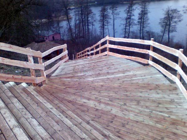 Drewniane schody z balustradą prowadzące w dół zbocza w kierunku jeziora, wykonane z desek ułożonych w wachlarz, widok z góry.