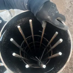 Zbrojenie pionowe w szalunku cylindrycznym, przygotowane do zalania betonem, widok z góry, rękawica robocza w kadrze.