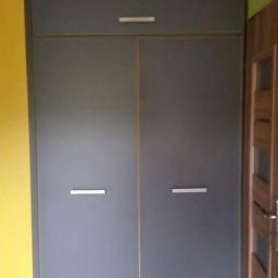 Meble z Pomysłem - Szara szafa wnękowa z żółtym elementem obok, z minimalistycznymi uchwytami i cienkimi, pionowymi, żółtymi paskami między drzwiami i elementami szafy.