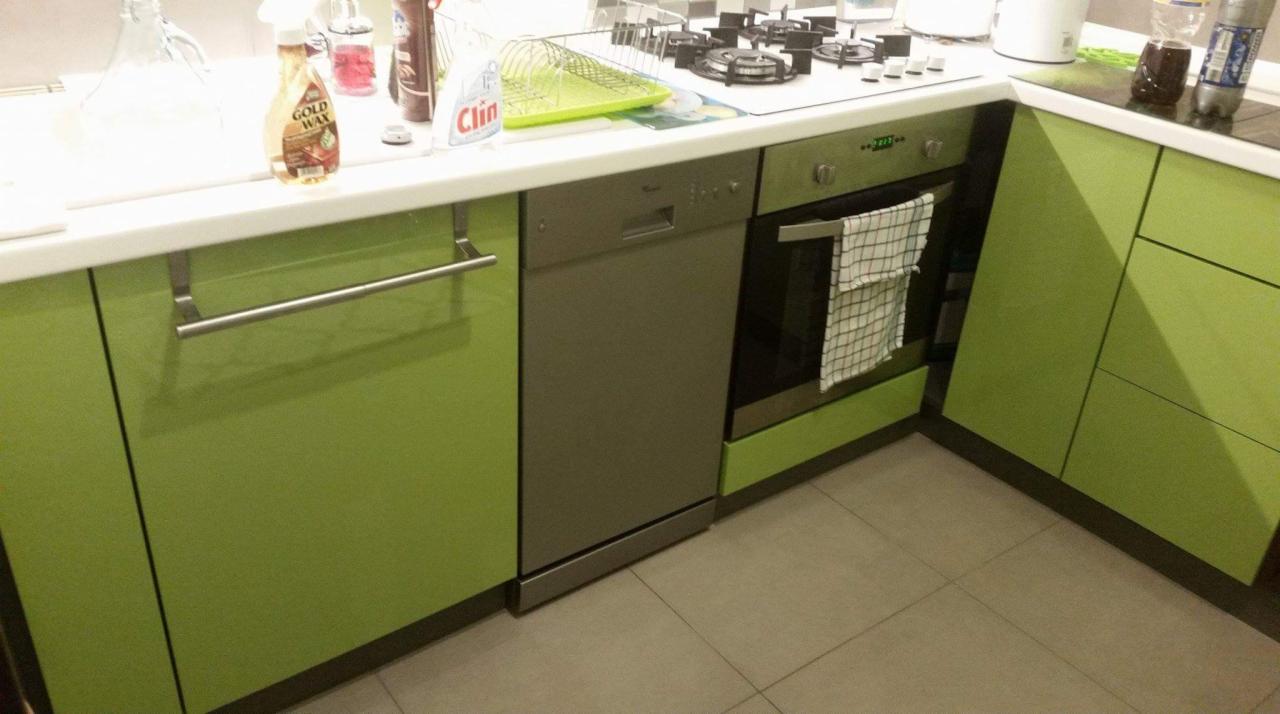 Fragment kuchni z zielonymi szafkami na wymiar, srebrną zmywarką i piekarnikiem, na blacie widoczne środki czystości i naczynia.