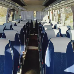 Wnętrze autobusu z rzędami niebieskich foteli z białymi zagłówkami, widok z przodu na puste przejście.