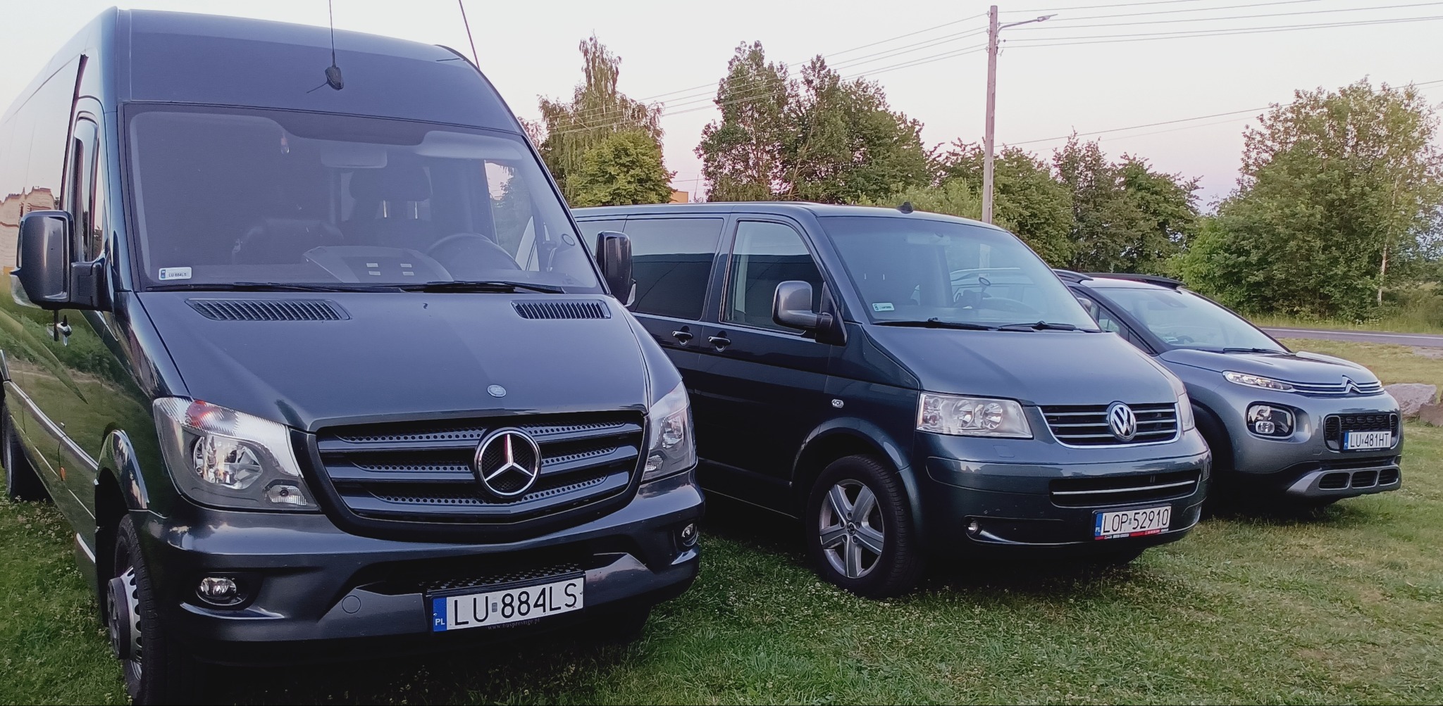 Flota pojazdów: Mercedes Sprinter, Volkswagen Transporter i Citroen C4 Cactus, zaparkowane na trawie.