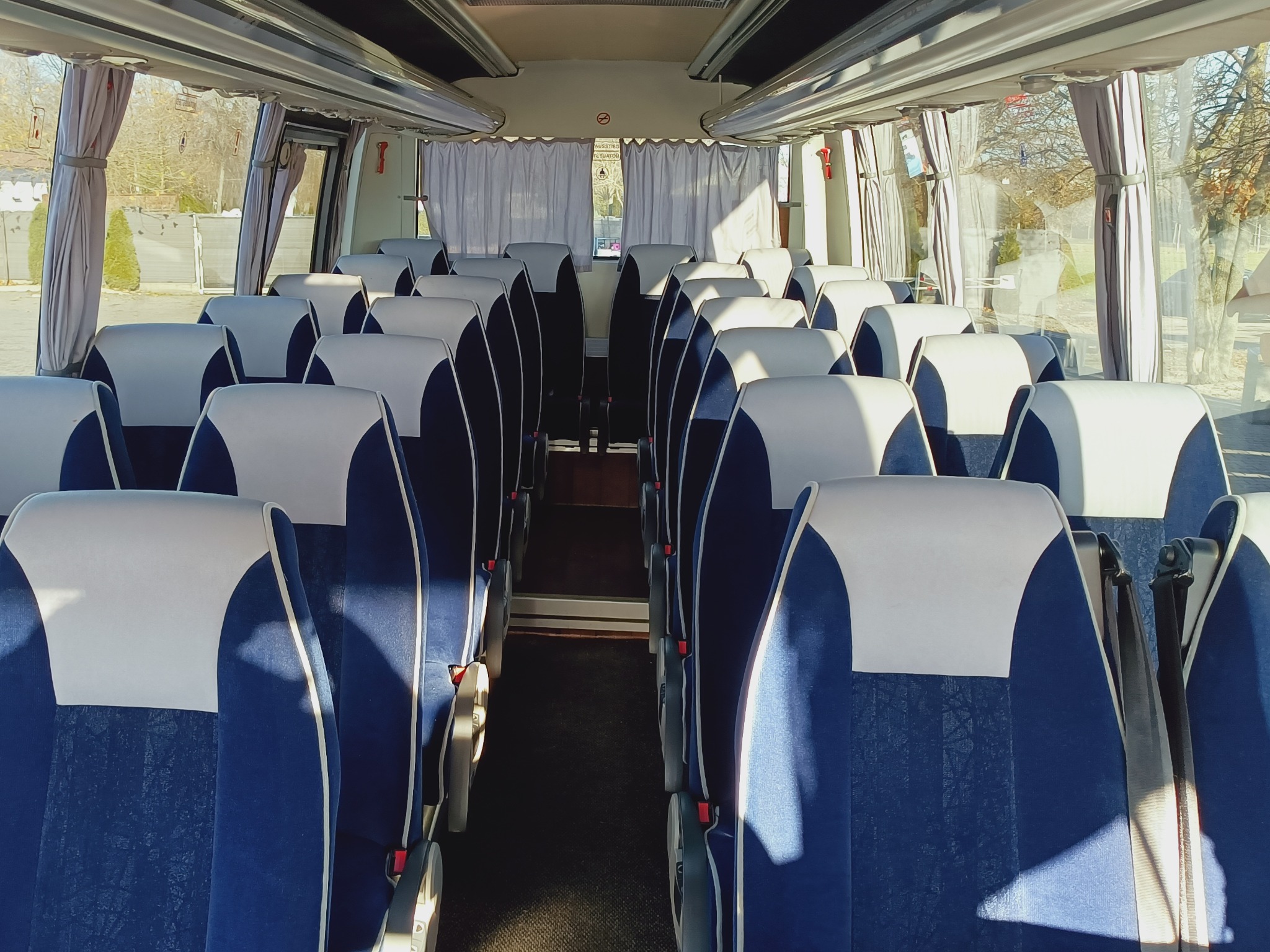 Wnętrze autobusu z rzędami niebieskich foteli z białymi zagłówkami, widok z przodu na puste przejście.