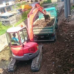 Czerwona minikoparka na gąsienicach nabiera ziemię do zielonej ciężarówki na placu budowy w górskim otoczeniu.