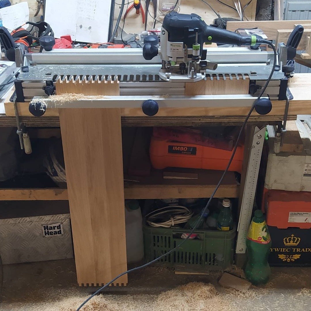 Frezarka górnowrzecionowa Festool w warsztacie w Jordbro, przygotowująca drewniany element z wyfrezowanymi wpustami, widoczne wióry i narzędzia na półkach.