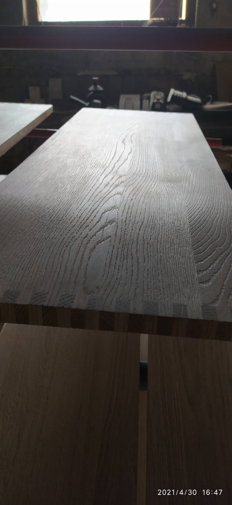 Blat drewniany z widocznymi połączeniami na krawędzi, o wyrazistym usłojeniu, leżący na konstrukcji w warsztacie.