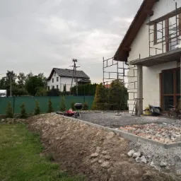 Budowa domu jednorodzinnego w Sosnowcu: ściany zewnętrzne w trakcie ocieplania, widoczne rusztowania, teren wokół domu w trakcie przygotowywania.