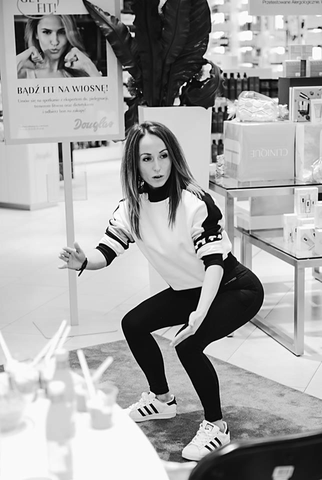 Kobieta w sportowym stroju robi przysiad w sklepie Douglas, obok plakat 'Bądź Fit na wiosnę!'