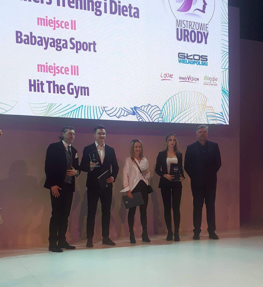 Grupowe zdjęcie osób na scenie podczas gali wręczenia nagród Mistrzowie Urody, z widocznym logotypem Głos Wielkopolski i Fitexpo w tle.