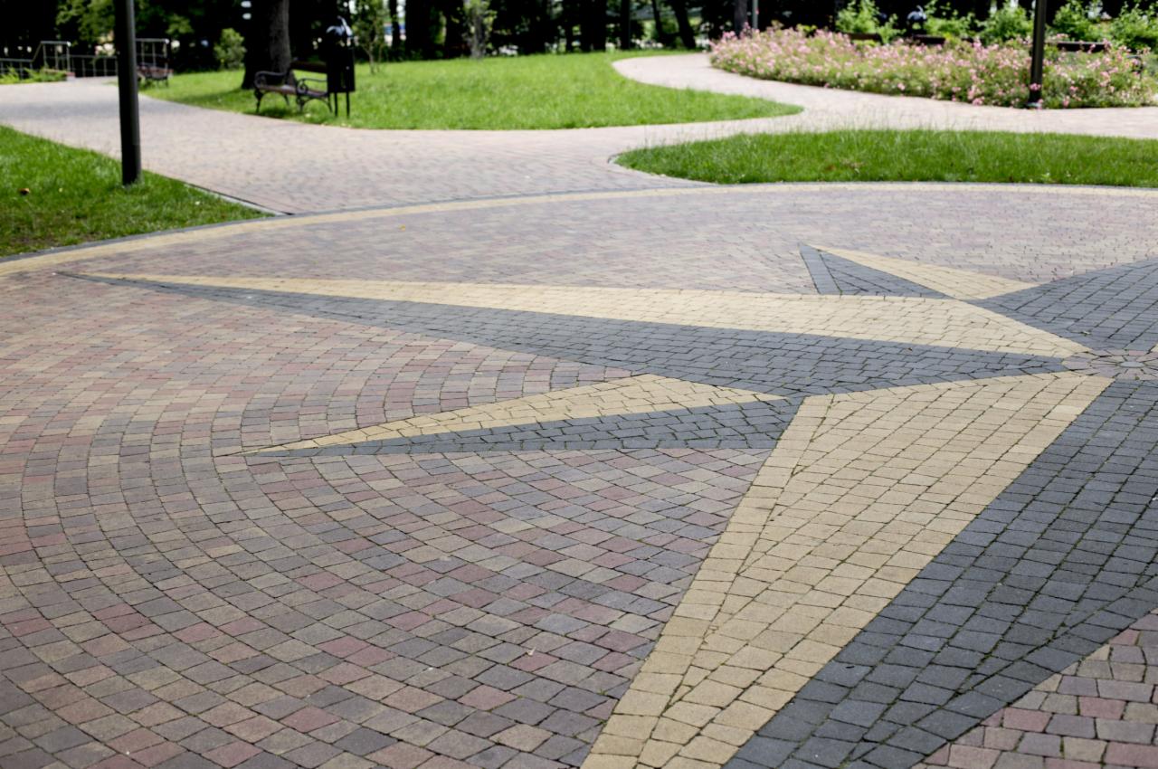 Ułożona kostka brukowa w kształcie gwiazdy na placu w parku, z widocznymi ścieżkami i zielenią w tle.
