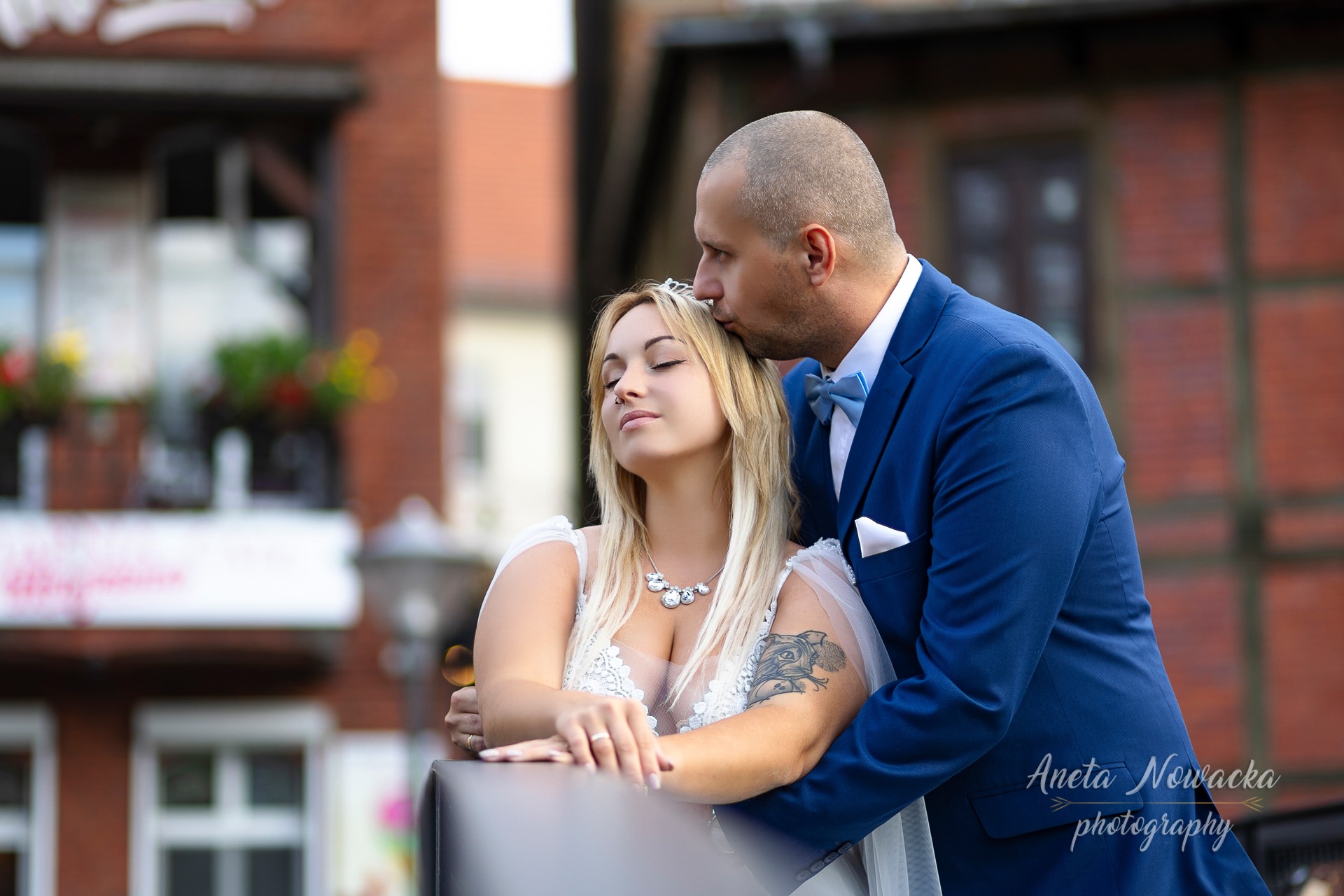 Pocałunek w czoło panny młodej z tatuażem na ramieniu, w Bydgoszczy, na tle ceglanej architektury.