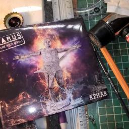 Letcom Tomasz Kubiak - Dwa albumy muzyczne zespołu Jarus Pure Rock n Roll Rehab leżące na zielonej macie do cięcia, obok narzędzi takich jak młotek, ołówek, pędzel i zakrętka od butelki.