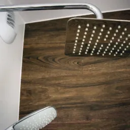 Nowoczesna kabina prysznicowa z chromowaną armaturą i deszczownicą na tle ściany z imitacją drewna.