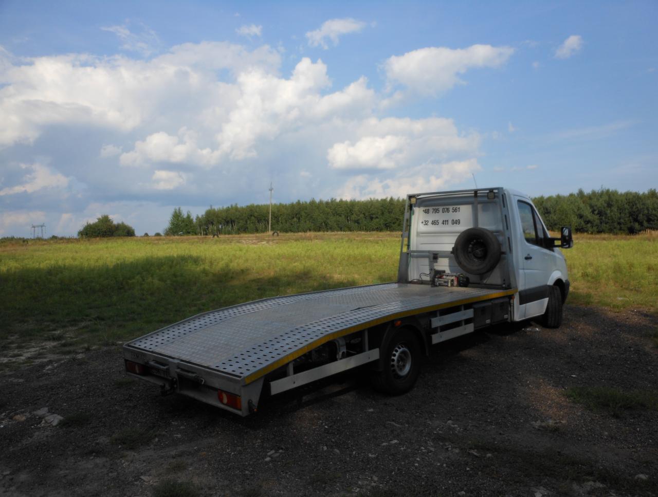 Laweta na tle zielonego pola i błękitnego nieba z chmurami. Na kabinie numery kontaktowe.