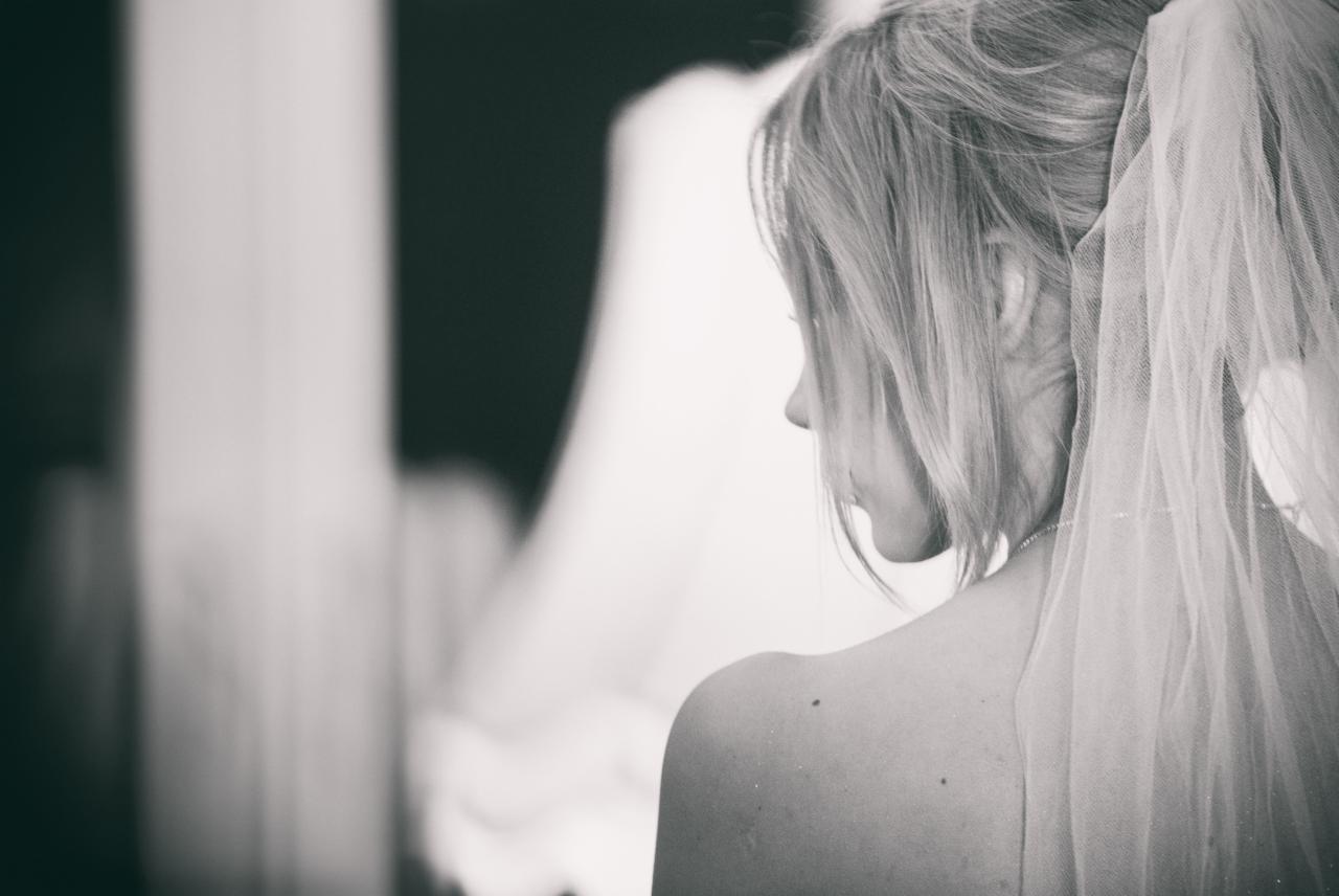 Czarno-białe zdjęcie panny młodej z welonem, widok z profilu na plecy i włosy upięte w kok, delikatny makijaż.