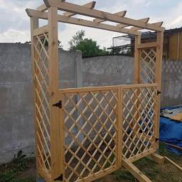 GREG-STOL Mała Stolarnia - Surowa drewniana konstrukcja z kratownicą, prawdopodobnie wejście do ogrodu, jeszcze nie wykończona, z widocznymi elementami podtrzymującymi i betonowymi podstawami.