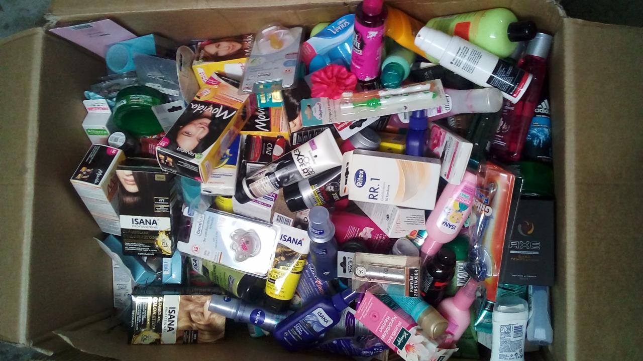 Karton wypełniony różnorodnymi produktami higienicznymi i kosmetykami różnych marek, w tym Isana, Nivea, Axe, Movida i Venus, widoczne opakowania farb do włosów, żele pod prysznic, dezodoranty...