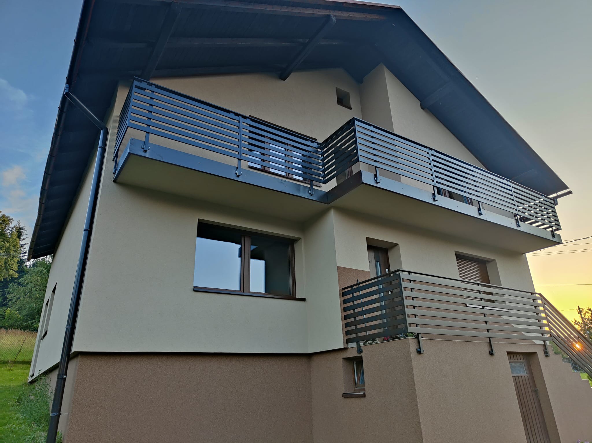 Nowoczesny dom z balkonami zabezpieczonymi poziomymi balustradami w kolorze antracytowym, widok z dołu na elewację dwukolorową.