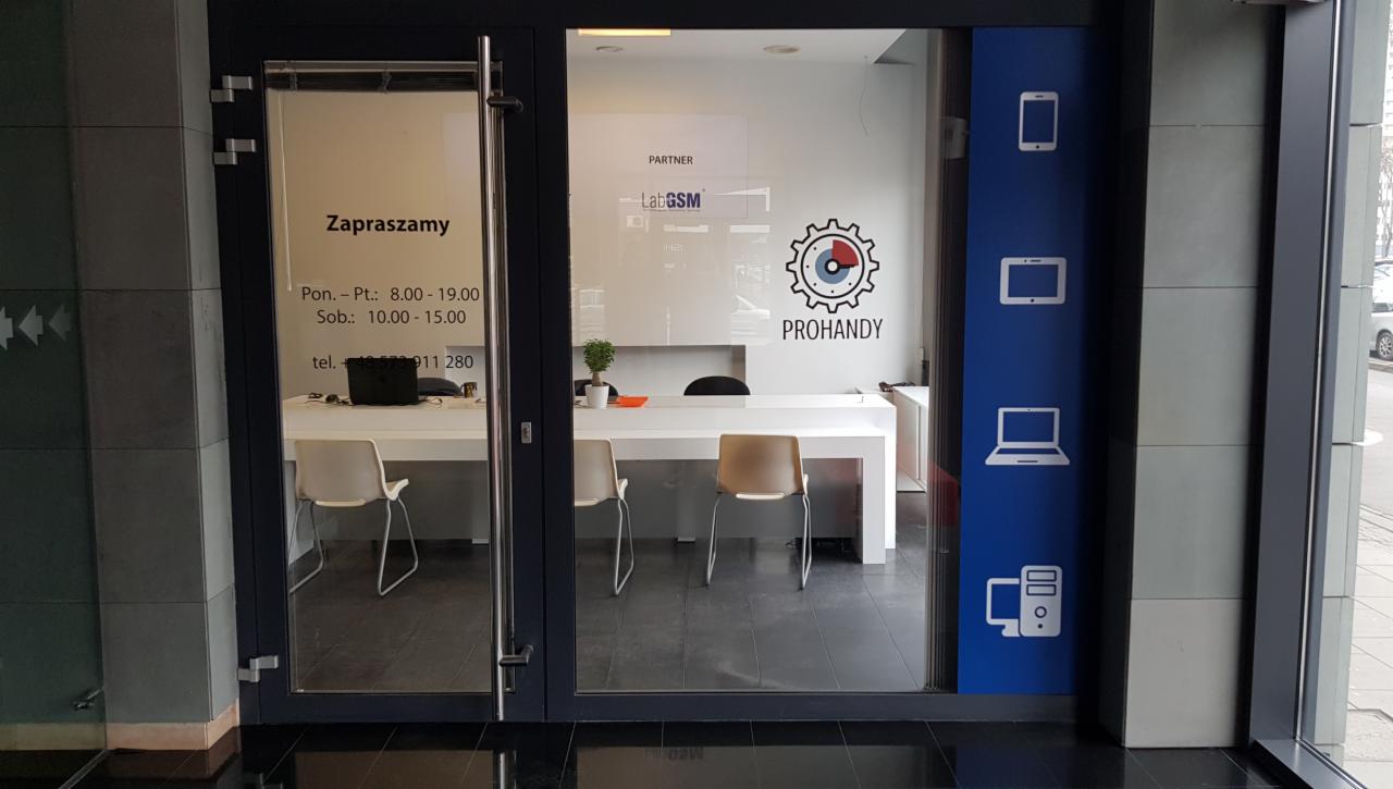 Wejście do serwisu z logo Prohandy, godziny otwarcia na szybie, grafiki smartfona, laptopa i komputera stacjonarnego na niebieskim panelu obok drzwi.