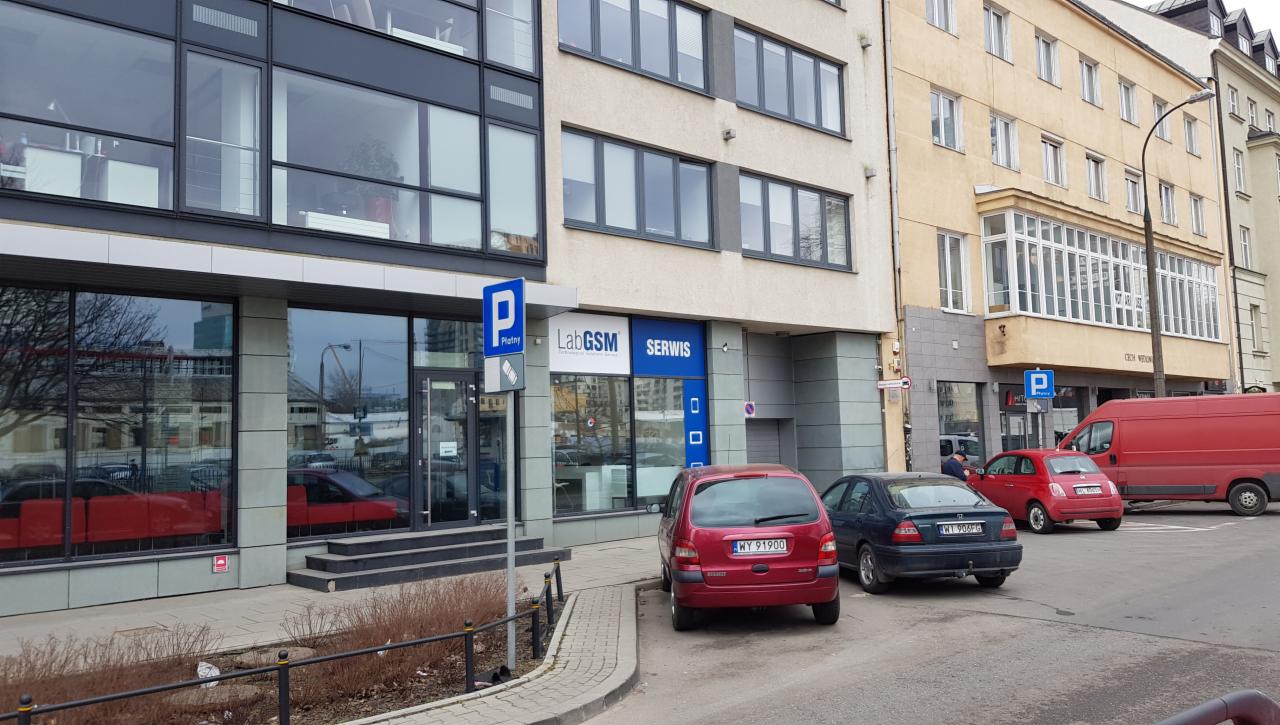 Fasada budynku z szyldem 'LabGSM Serwis' nad wejściem; zaparkowane samochody przed lokalem.