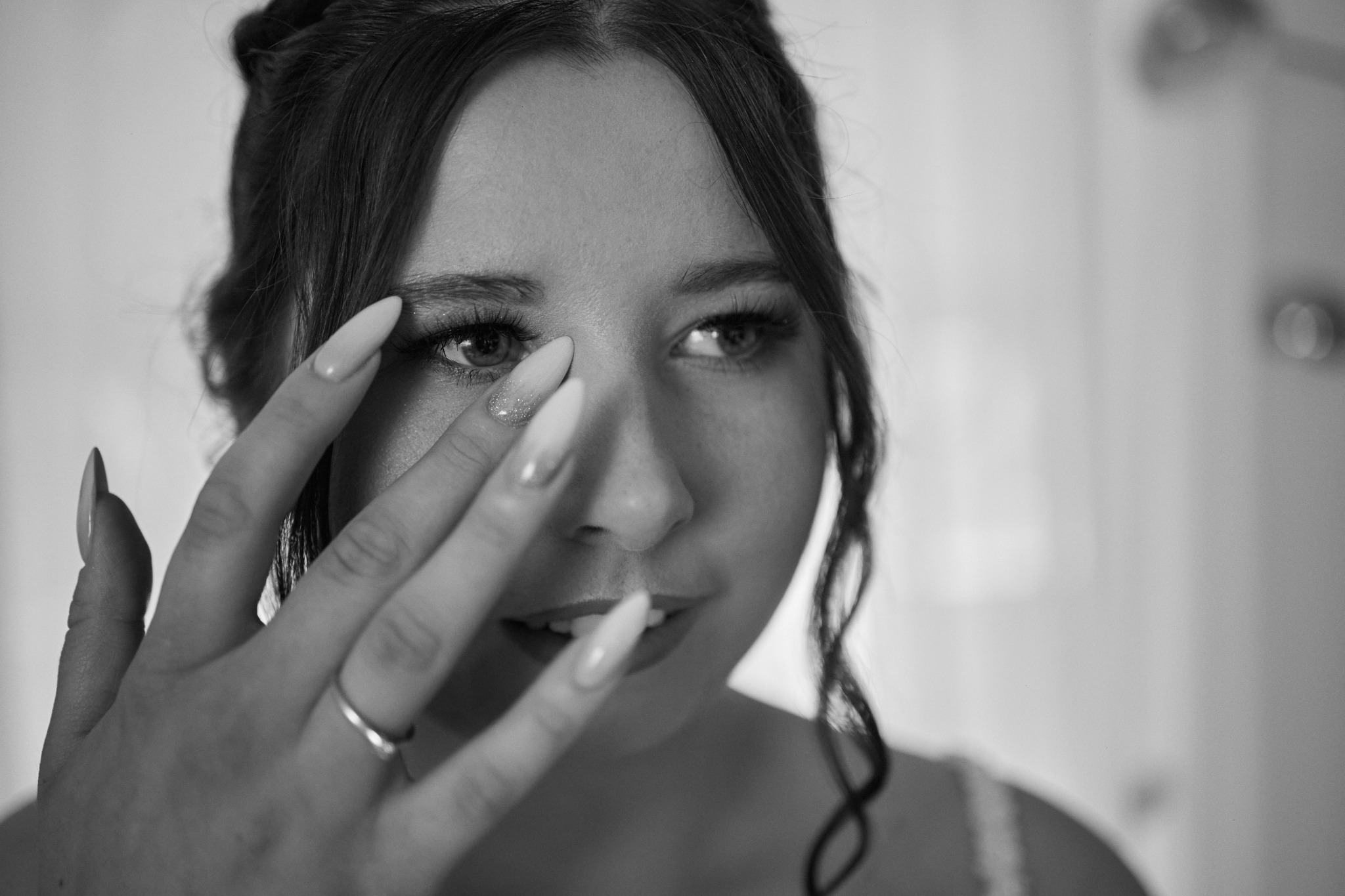 Portret zbliżeniowy kobiety z długimi, ozdobionymi paznokciami, delikatnym makijażem i upiętymi włosami, w czerni i bieli, z pierścionkiem na palcu.