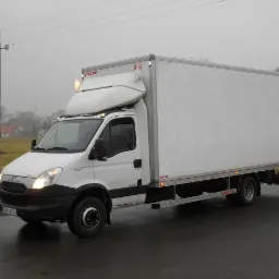 Biały samochód dostawczy Iveco Daily z zabudową kontenerową Unicar, zaparkowany na mokrym asfalcie w pochmurny dzień, widoczny numer rejestracyjny DW 1W235.