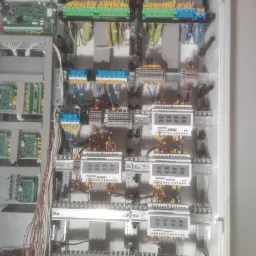 Wnętrze szafy sterowniczej z zamontowanymi modułami, listwami zaciskowymi i licznikami energii elektrycznej, widoczne kable w różnych kolorach.