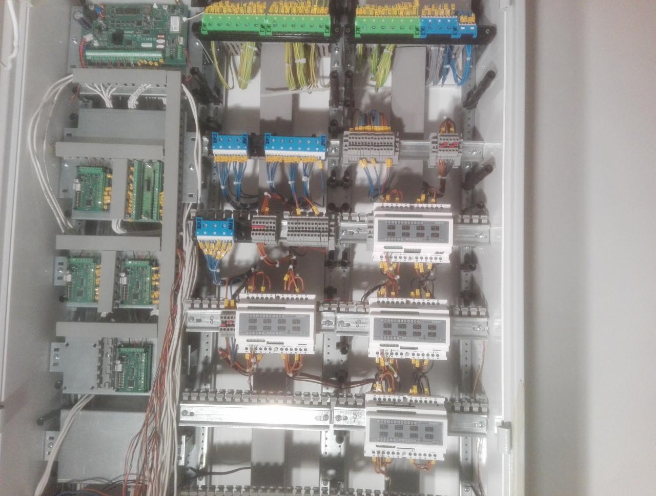 Wnętrze szafy sterowniczej z zamontowanymi modułami, listwami zaciskowymi i licznikami energii elektrycznej, widoczne kable w różnych kolorach.