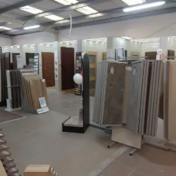 Ekspozycja w sklepie z różnymi modelami drzwi i paneli podłogowych na stojakach, widoczne różne kolory i wzory, oświetlenie sufitowe.