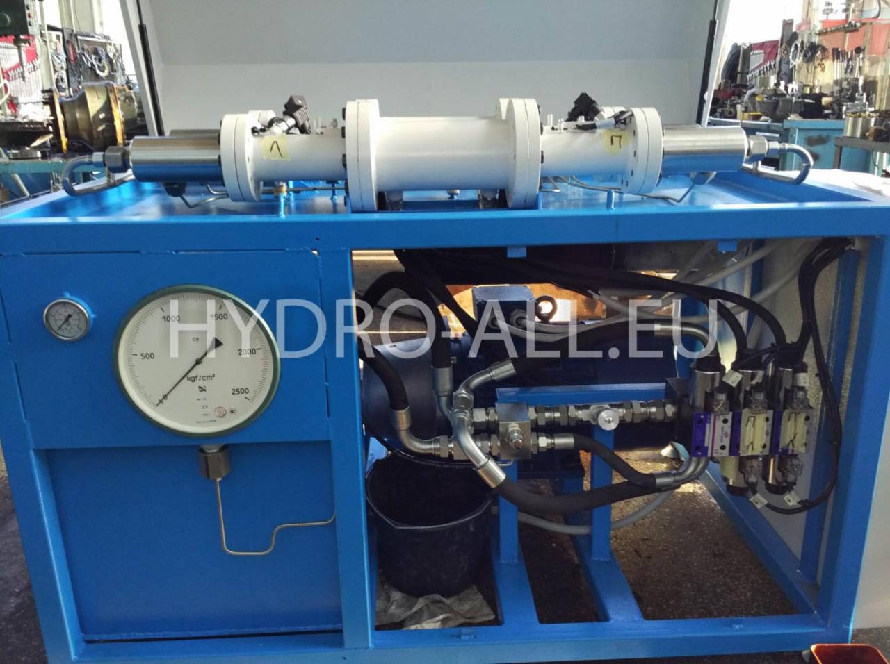Agregat hydrauliczny w niebieskiej obudowie z manometrem i przewodami, widoczne elementy stacji olejowej.