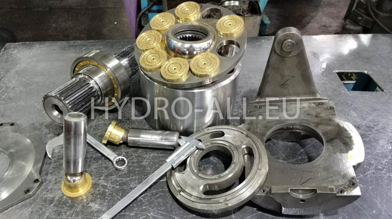 Rozłożony na metalowym stole zespół części zamiennych do wózków widłowych, w tym cylinder z tłokami, wał napędowy, suwmiarka i klucze.