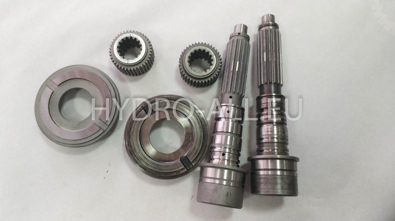 Zestaw metalowych części zamiennych, w tym dwa wały z frezami, dwa koła zębate oraz dwa pierścienie, ułożonych na jasnym tle.