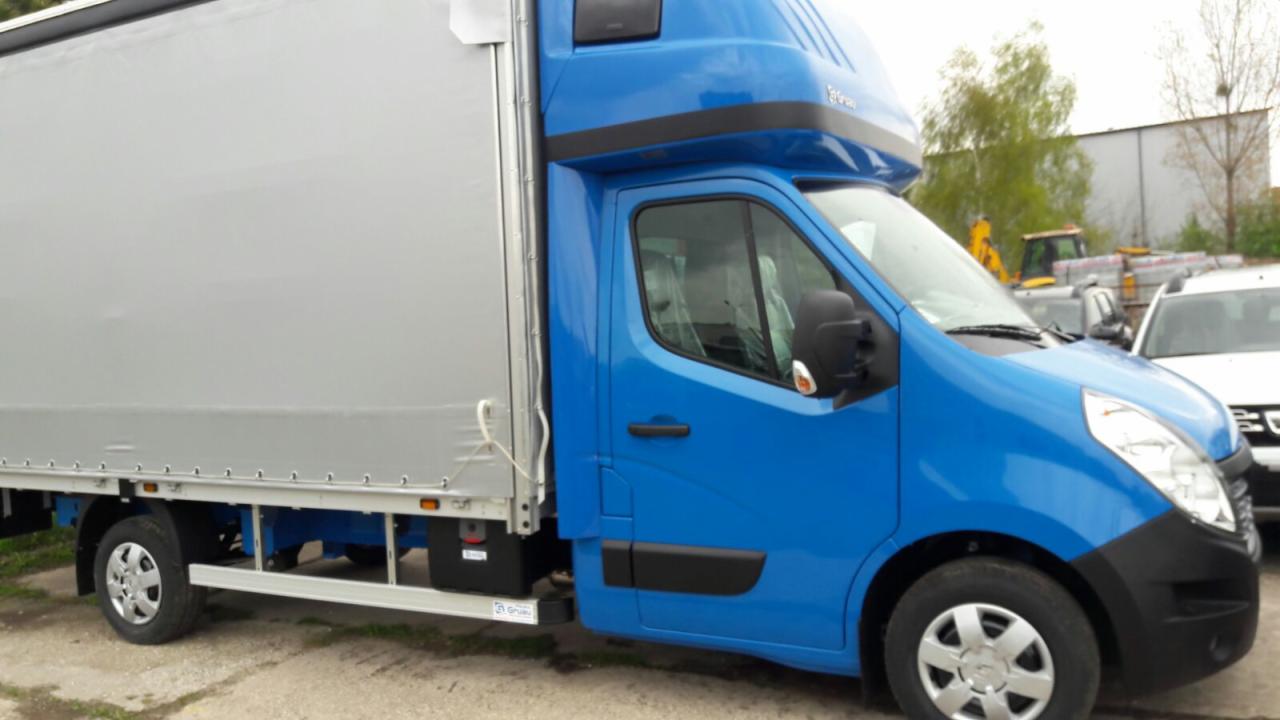 Niebieski samochód dostawczy z plandeką na parkingu, z widocznym sprzętem budowlanym w tle.