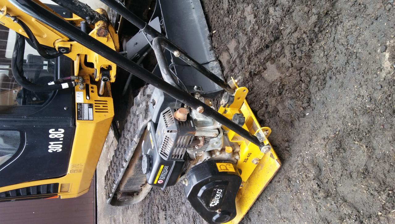 Żółta zagęszczarka gruntu marki Beko obok minikoparki Caterpillar 301.8C na ubitym, ciemnym gruncie.