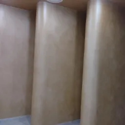 Beżowe, zaokrąglone ściany działowe z gładzią w nowoczesnym biurze, widoczne oświetlenie sufitowe.