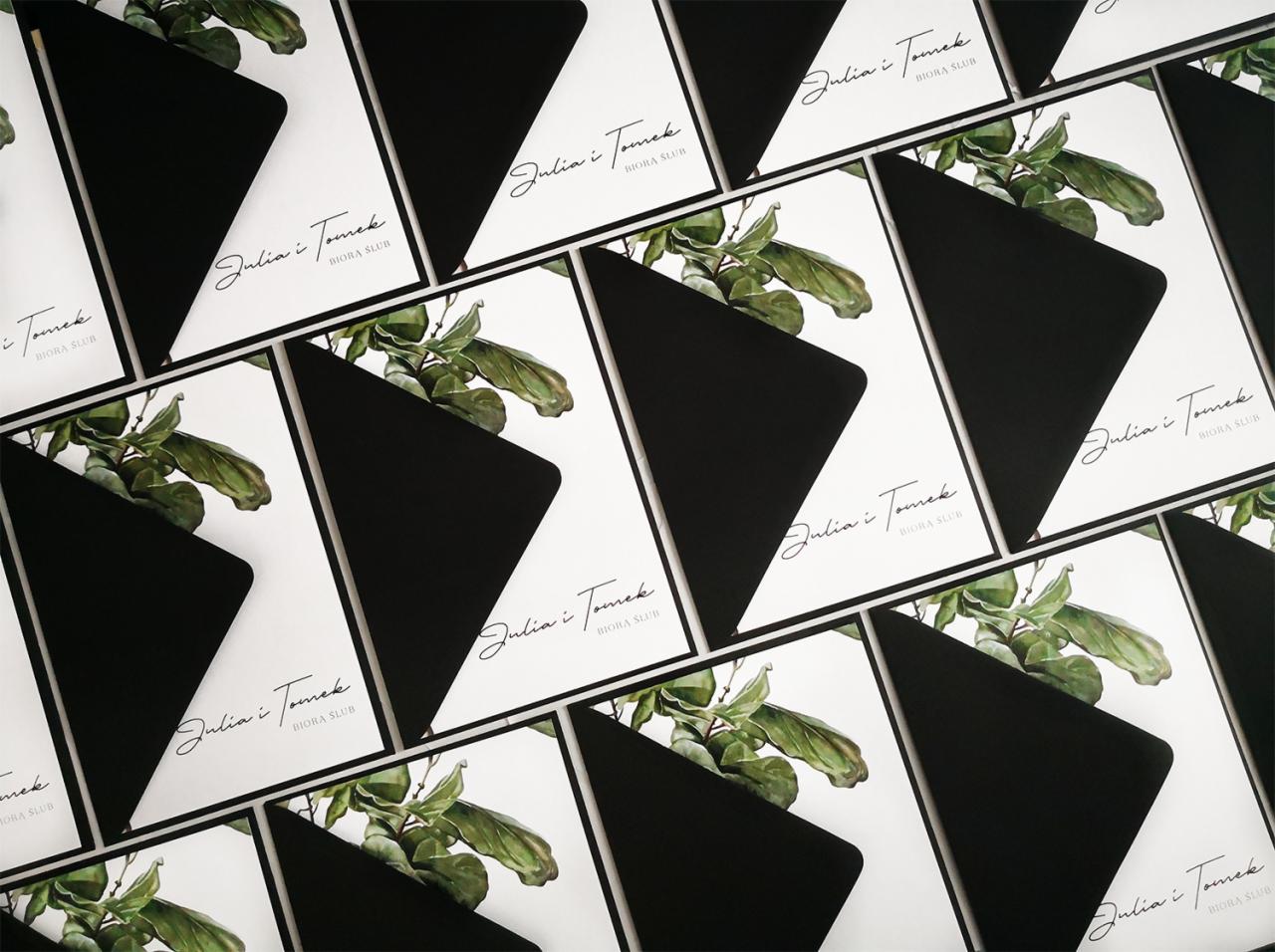 Stos wizytówek ślubnych z imionami 'Julia i Tomek' oraz subtelną akwarelą przedstawiającą zielone liście, umieszczonych w czarnych kopertach z trójkątnym zamknięciem.