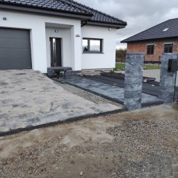 MarekSzałacki - Ułożona kostka brukowa na podjeździe i chodniku w Prusinowicach. Widoczne słupki z kostki i fragment domu z garażem. Prace brukarskie w toku.