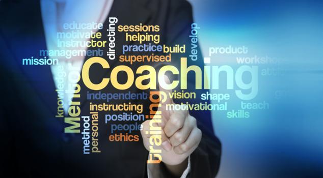 Dłoń wskazująca na słowo Coaching otoczone innymi słowami związanymi z rozwojem osobistym i edukacją, na niebieskim tle.