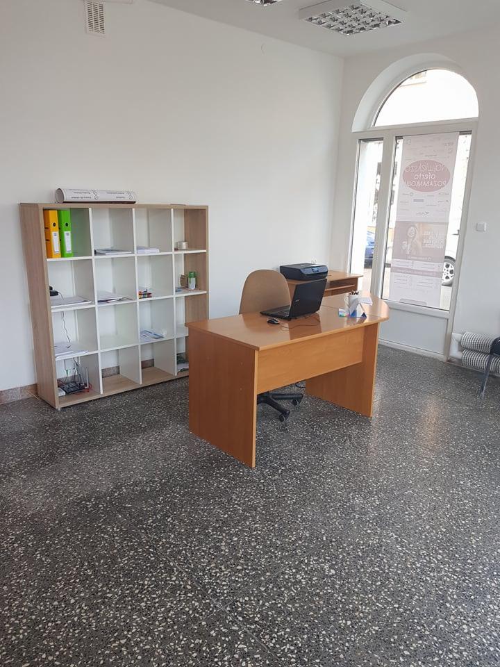 Biuro z biurkiem, krzesłem, regałem i oknem łukowym, widok na laptopa i drukarkę na biurku.