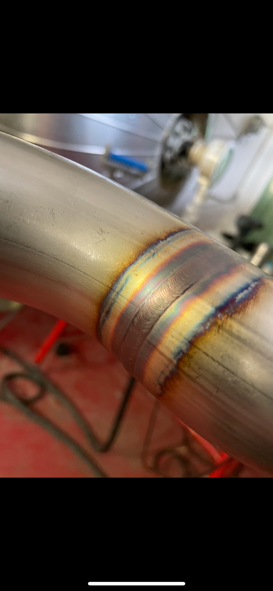 Precyzyjne spoiny na zakrzywionym, metalowym elemencie, z widocznymi tęczowymi przebarwieniami termicznymi.