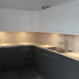 Nowoczesna kuchnia z szarymi szafkami dolnymi i białymi górnymi, podświetleniem LED pod szafkami, heksagonalnymi płytkami na ścianie i srebrną baterią.