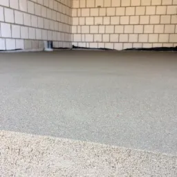 Świeżo wylana, szara posadzka na podkładzie z folii, widoczne ściany z białego bloczka betonowego i wystające kable.