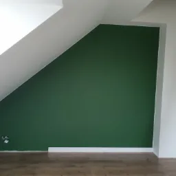 Pomieszczenie na poddaszu po świeżym pomalowaniu ściany na zielono, widoczne gniazdka elektryczne, listwa przypodłogowa i fragment drabiny.